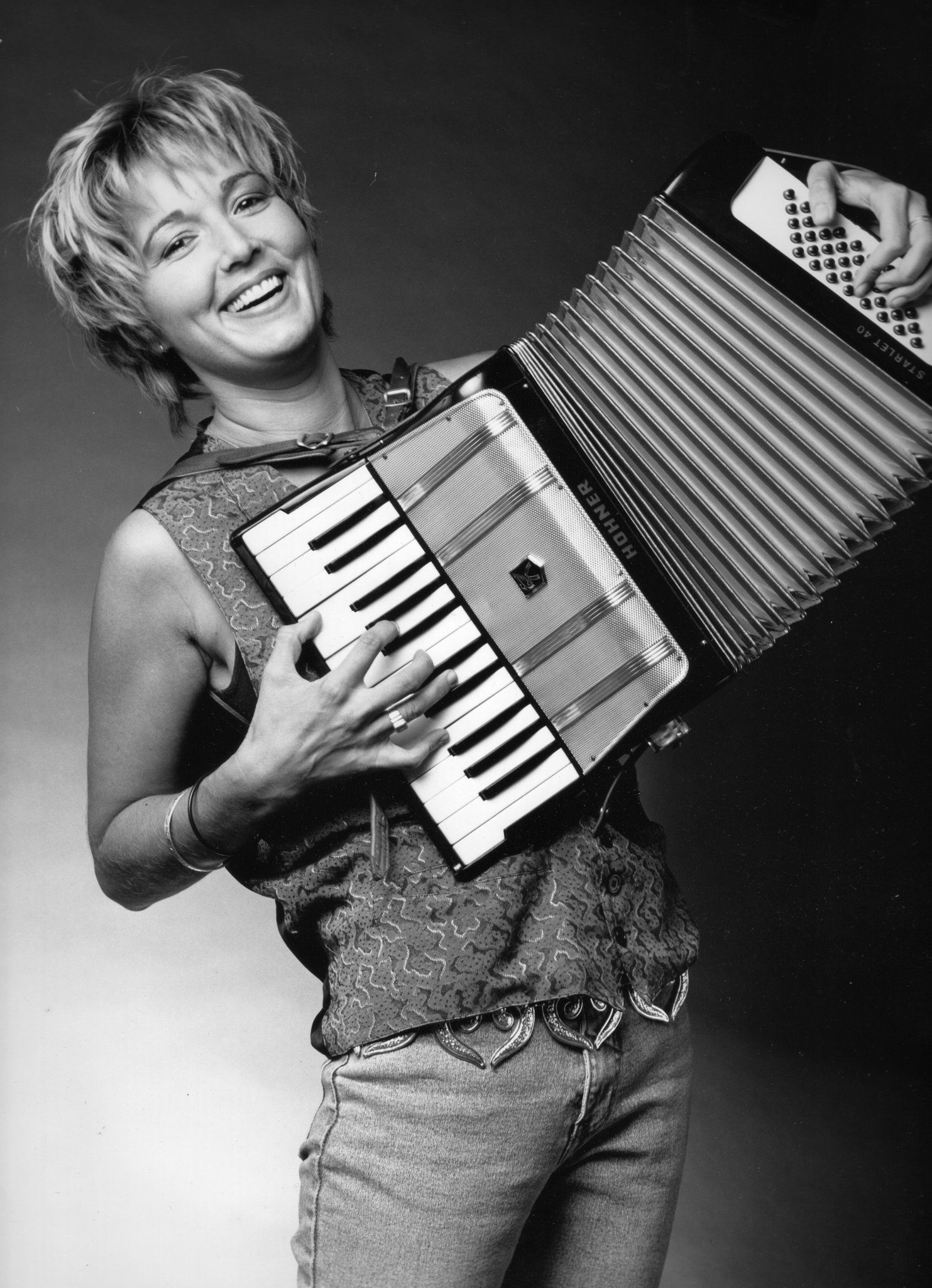 Debra Peters smiling while playing the piano accordion – 1992 publicity postcard