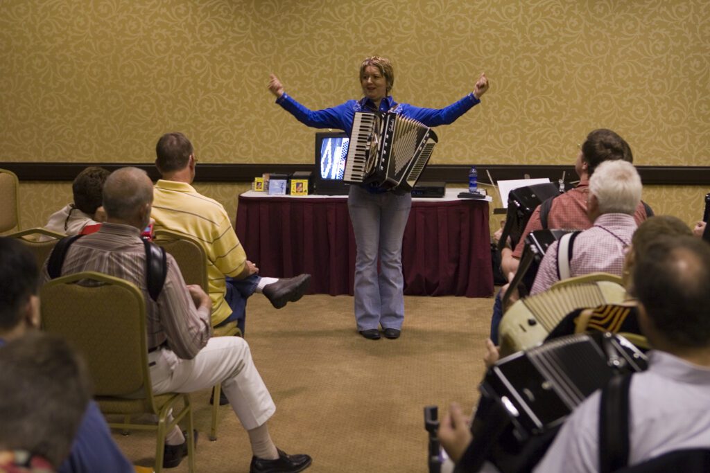 Debra Peters teaching an accordion workshop with arms outstretched to students at the National Accordion Association